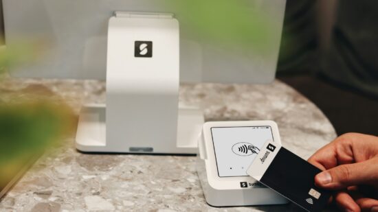A SumUp Solo card reader is being used to make a contactless payment with a SumUp card. The device is placed on a sleek, modern marble counter, enhancing the overall minimalist and professional aesthetic. The SumUp POS system behind the card reader emphasizes the streamlined and easy-to-use technology, ideal for cafes, boutiques, and other small businesses that value both function and design. This setup reflects a commitment to modern payment solutions with a stylish touch.
